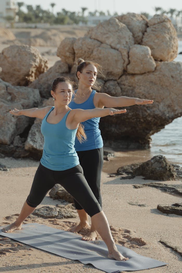 Two women in yoga poses on a beach showcasing outdoor fitness and mindfulness.